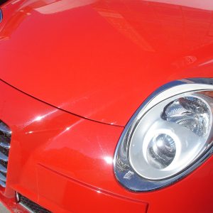Close-up of the red car's front end showing the headlight and Alfa Romeo badge on the grille