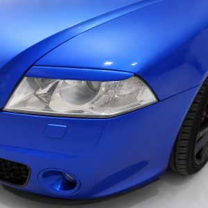 Close-up of a blue sports car's front left headlight and wheel.