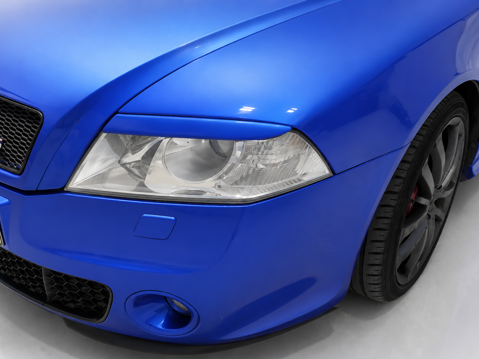 FR000110_1jpg - OPSHOLDERS Close-up of a blue sports car's front left headlight and wheel.