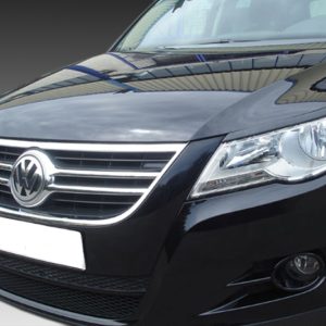 Close-up of the front end of a black VW car, showing the chrome grille and emblem with a white license plate area below.