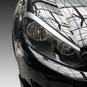 Close-up of a sleek black car's headlight and front end, with the glossy paint reflecting a glass- ceiling design.