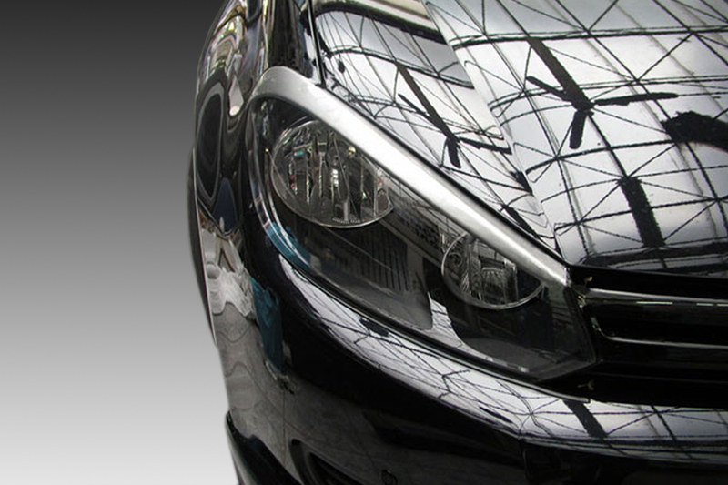FR000114_1jpg - OPSHOLDERS Close-up of a sleek black car's headlight and front end, with the glossy paint reflecting a glass- ceiling design.