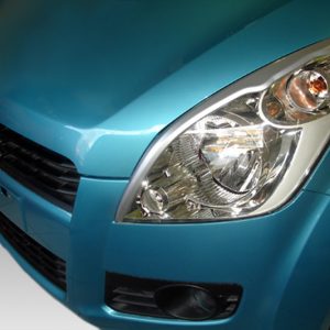 Close-up of a turquoise car's front end, highlighting the headlight and grille in a low-angle view of the car's front.