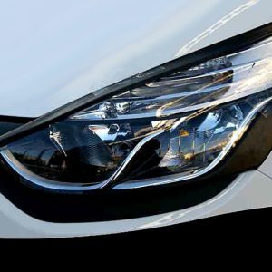 Close-up of a modern car headlight on a white vehicle, showing reflective surfaces and trim.