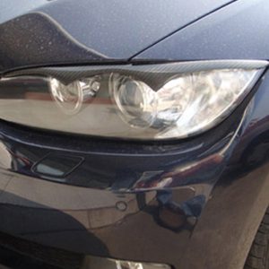 Close-up of a dark blue car's front left headlight and bumper, showing the headlight unit and nearby fender with reflections in the paint.