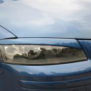 Close-up of a blue car's front left headlight and bumper area