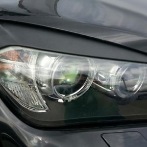Close-up of a dark gray car headlight assembly, showing projector lens, reflectors, and a clear cover.