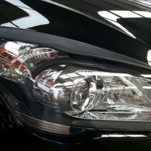 Close-up of a car headlight on a glossy black vehicle, showing reflective surfaces and chrome details.