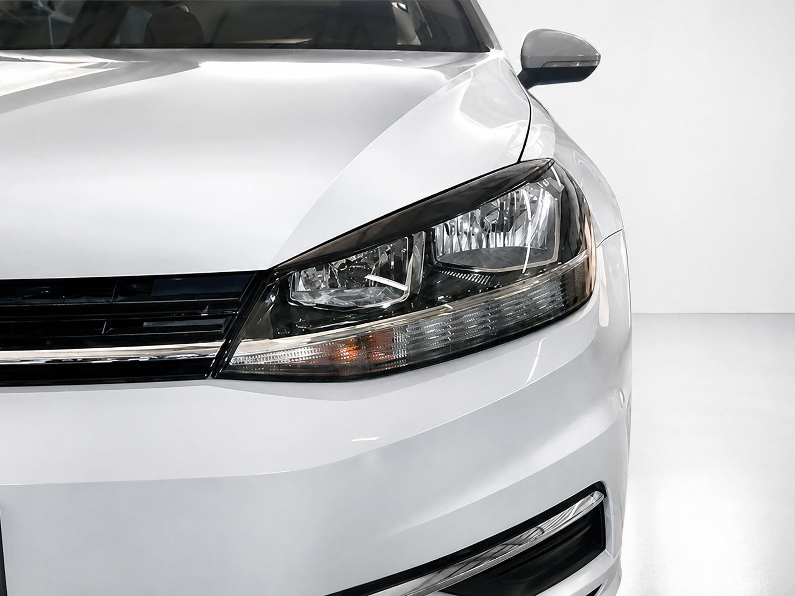 FR000144_1jpg - OPSHOLDERS Close-up of the front left corner of a white car, highlighting the headlight and grille area.