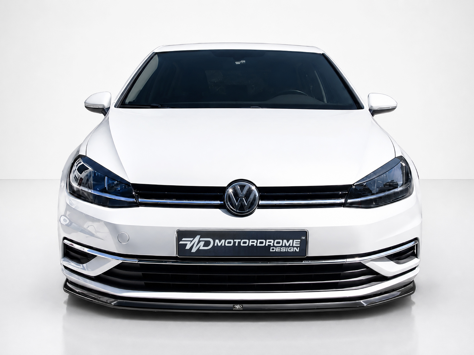 FR000144_2jpg - OPSHOLDERS Front view of a white Volkswagen car in a studio setting, showing the grille, emblem, and headlights against a light background.