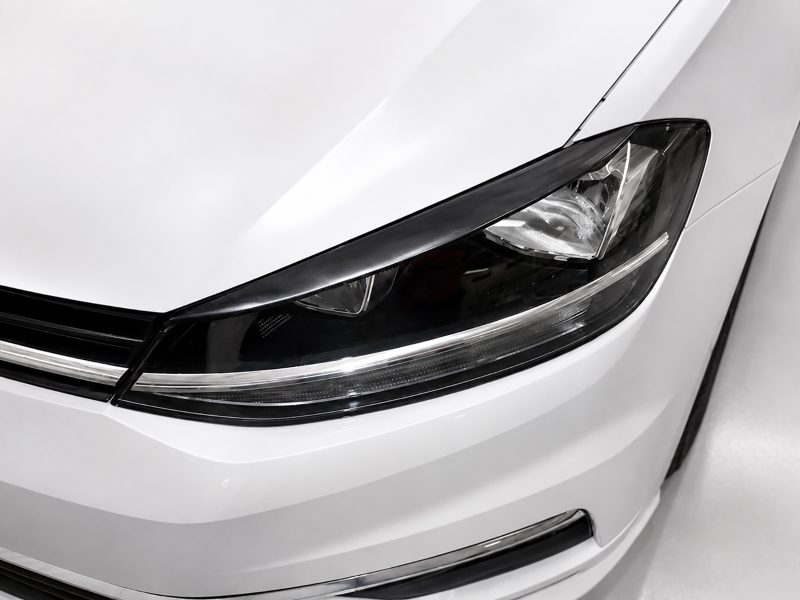 FR000144_3jpg - OPSHOLDERS Close-up of a white car's headlight and front bumper area.