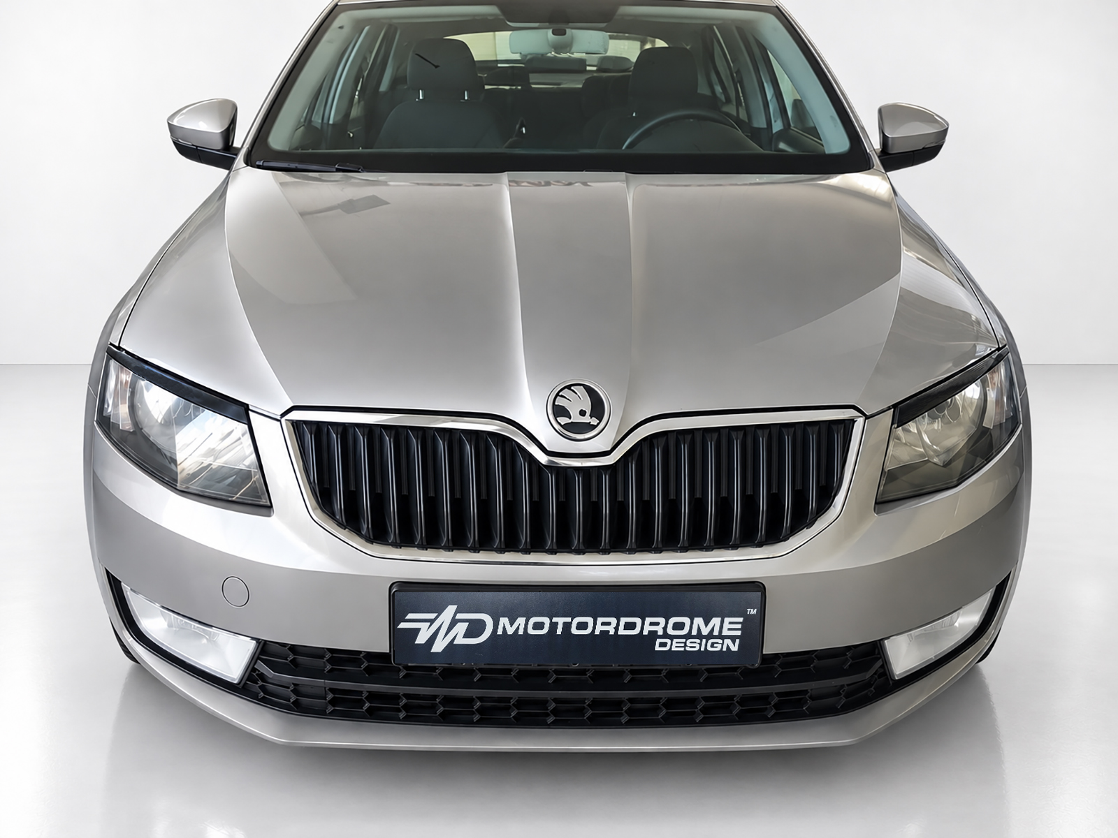 FR000146_2jpg - OPSHOLDERS Front view of a silver car in a showroom with a prominent black grille and Skoda emblem on the hood badge.