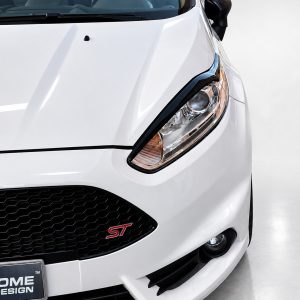 Close-up of a white Ford car front: prominent headlight, honeycomb grille, and ST badge visible near the lower grille.