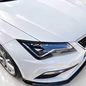 Close-up of a silver car's front end showing the headlight, grille, and curved hood from a low angle.