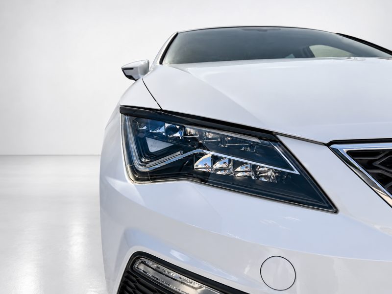 Close-up of the left headlight and front fender of a white car, showing a sharp LED daytime running light.