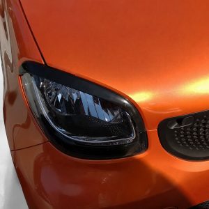 FR000153_2jpg - OPSHOLDERS Close-up of an orange car front corner featuring a headlight, black trim, and honeycomb grille area.