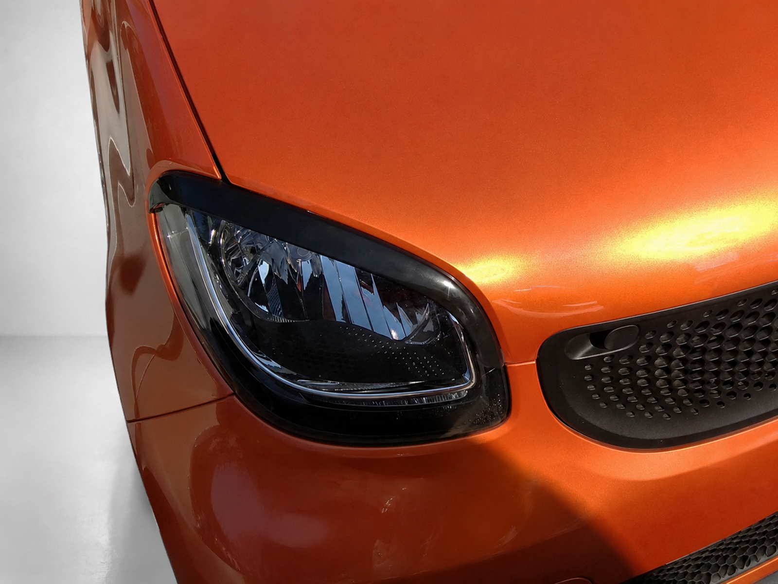 FR000153_2jpg - OPSHOLDERS Close-up of an orange car front corner featuring a headlight, black trim, and honeycomb grille area.