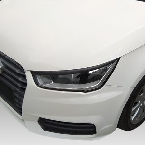 Front-left view of a white Audi car showing the grille, headlight, and front wheel in a studio setting