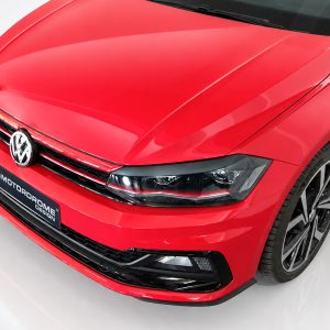 Red Volkswagen car front end with emblem, headlight, and large alloy wheel visible on the right.