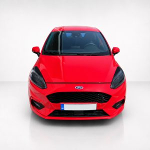 Front view of a red Ford car in a bright studio setting, facing the camera, with a black hex grille and Ford emblem visible on the grille.