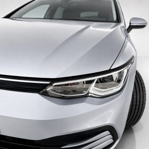 Close-up of the front left side of a silver car, highlighting the headlight and curved hood.