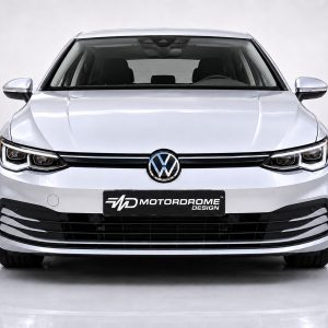 Front view of a silver Volkswagen with prominent logo, chrome grille, and bold bumper in a studio setting, license plate reads Motordrome Design.