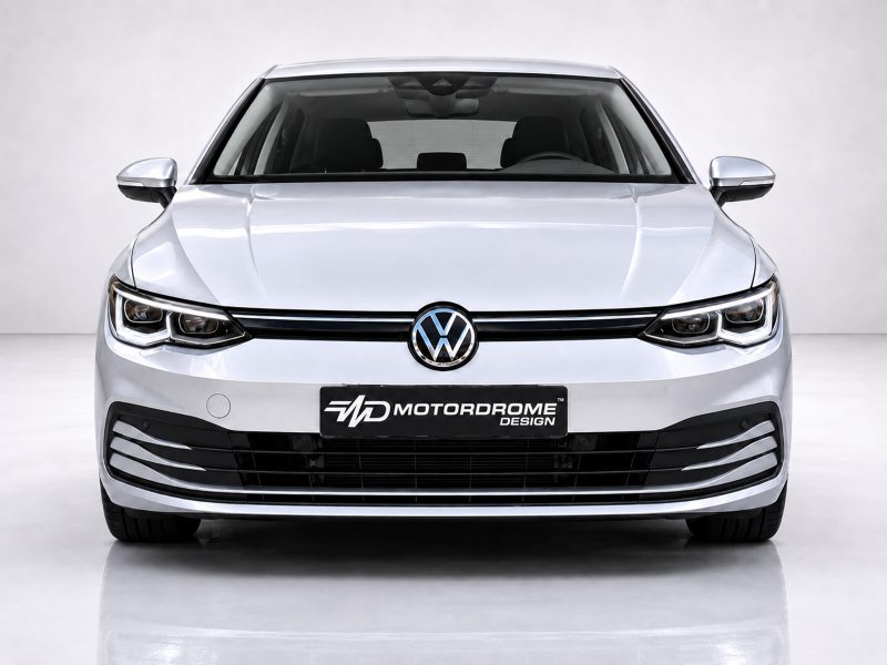 Front view of a silver Volkswagen with prominent logo, chrome grille, and bold bumper in a studio setting, license plate reads Motordrome Design.