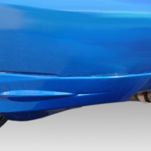 Close-up of a blue car's lower side panel near the rear wheel with a visible exhaust tip beneath.