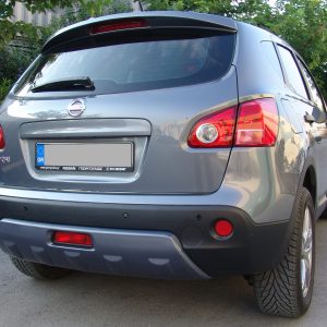 Rear view of a gray Nissan SUV parked on a street with greenery in the background and a Greek license plate visible on the tailgate.