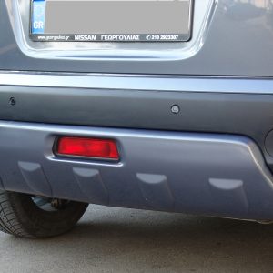 Rear view of a gray Nissan Qashqai showing the bumper, parking sensors, red taillights, and wheel at the lower left.