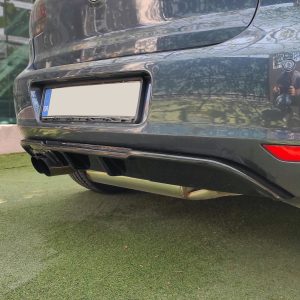 Rear of a dark SUV with a blank license plate, reflecting surroundings and the photographer on the shiny bumper surface.