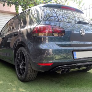 K128-006_2jpg - OPSHOLDERS Rear three-quarter view of a dark gray Volkswagen SUV parked on green artificial turf beside a beige wall and closed garage door, with reflections on the rear window.