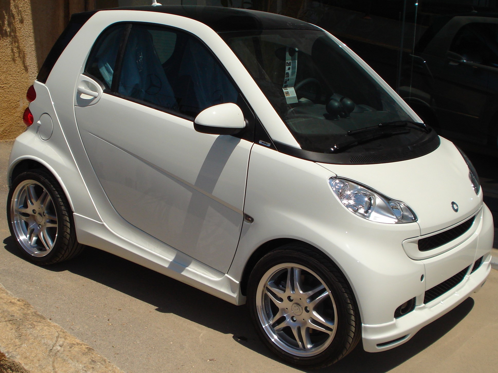 K135-003_1jpg - OPSHOLDERS White compact car parked on a driveway, shown from the front-right side with alloy wheels and a black roof rail.