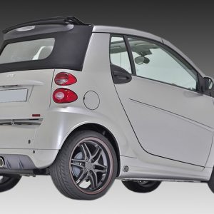 Silver Smart car, rear-left angle with black soft top, two exhaust, and alloy wheels visible on a gray gradient background