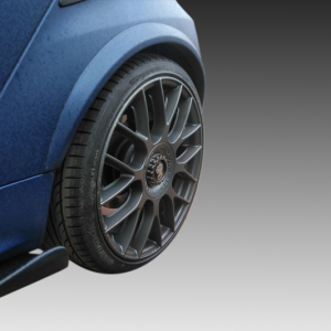Close-up of a blue car's front wheel with a multi-spoke dark alloy rim and tire, against a gray gradient background.