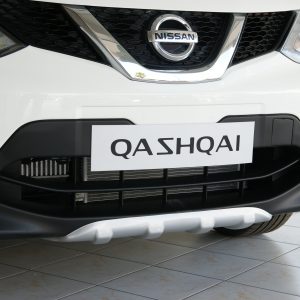 Front view of a white Nissan Qashqai showing the grille, emblem, and a license plate reading QASHQAI