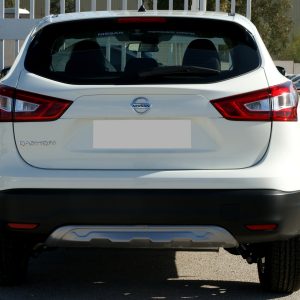 Rear view of a white Nissan Qashqai in a parking lot, showing red tail lights and the Nissan badge on the hatch.