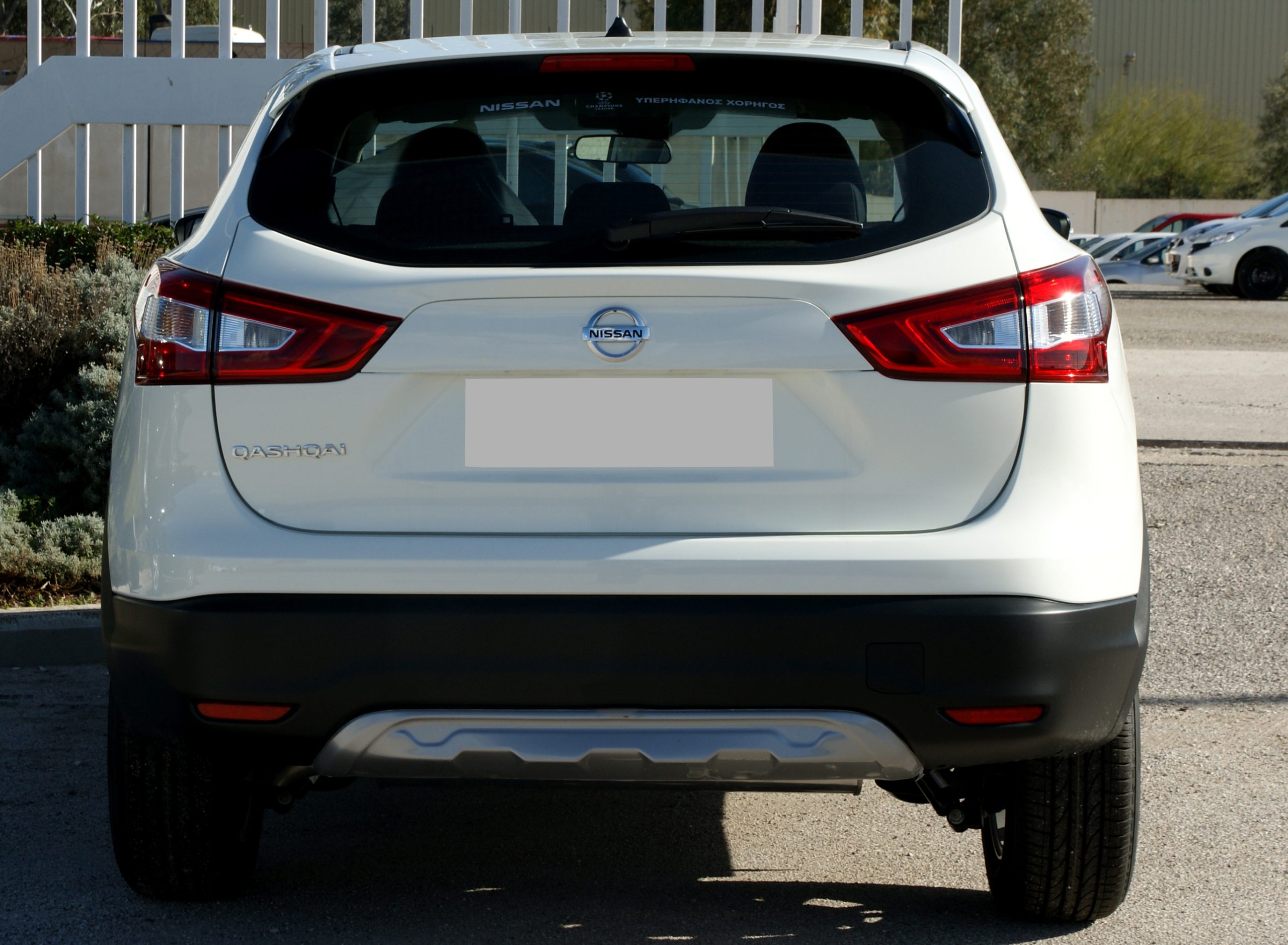 SONY DSC - OPSHOLDERS Rear view of a white Nissan Qashqai in a parking lot, showing red tail lights and the Nissan badge on the hatch.
