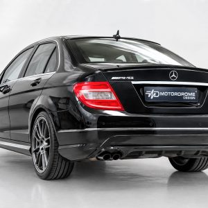 Rear-left three-quarter view of a black Mercedes-Benz AMG sedan, showing red taillights and MD Motorrome Design license plate area.