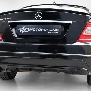 Rear view of a black Mercedes-Benz AMG with a Motordrome Design plate on the trunk.