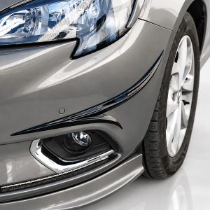 Close-up of a silver car front showing the headlight, bumper, and curved chrome accents beside the front wheel.