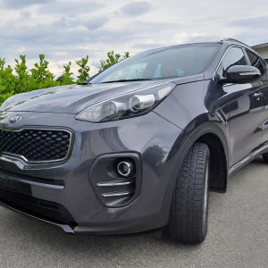 Front three-quarter view of a gray Kia SUV parked on a driveway with green hedge in the background.