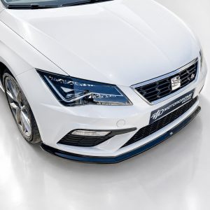 Front-left view of a white sports sedan showing its headlight, grille, and logo badge in a glossy showroom setting.