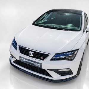 White sedan viewed from the front-left, showing the grille and sleek headlights in a studio setting with a glossy floor.