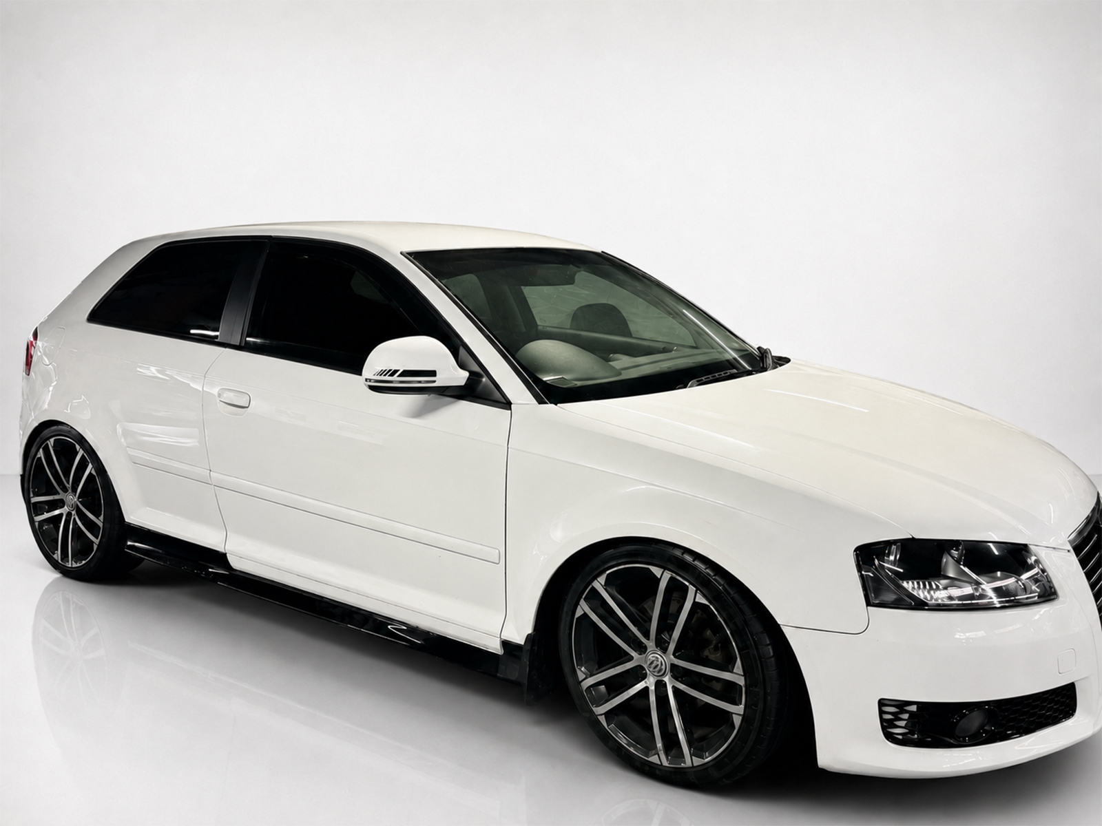 K151-003_2jpg - OPSHOLDERS White sports sedan with large black alloy wheels parked on a glossy white surface, in a studio setting.