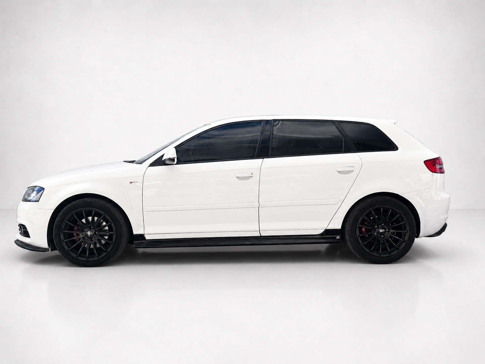K151-004_1jpg - OPSHOLDERS Side profile of a white station wagon with black alloy wheels and dark-tinted windows against a neutral backdrop, showroom style.