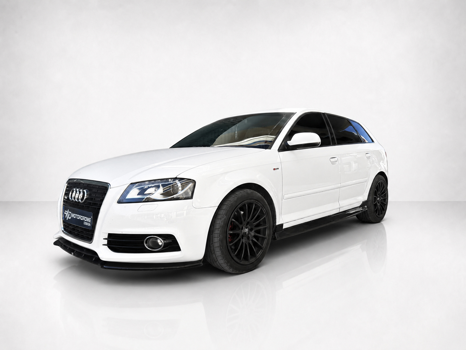 K151-004_2jpg - OPSHOLDERS White Audi sedan in a three-quarter front view with black multi-spoke wheels, photographed in a bright studio on a glossy floor.