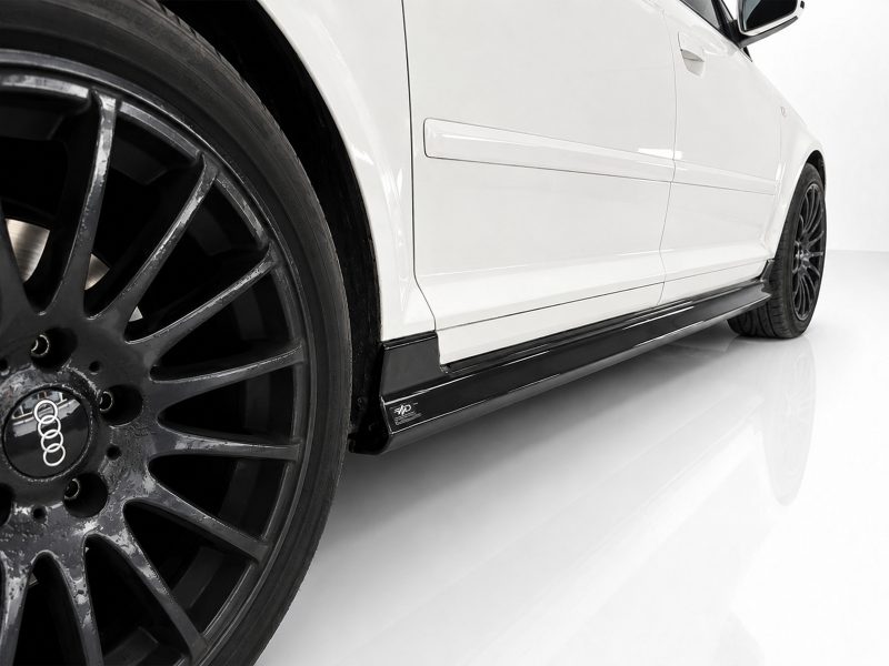 K151-004_4jpg - OPSHOLDERS White car side close-up with large black alloy wheel and sleek side skirt, Audi emblem on the rim visible