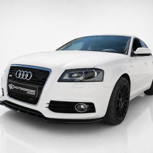 White Audi sedan in a studio, front three-quarter view with black grille and black alloy wheels.