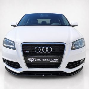 Front view of a white Audi sedan in a studio, showing the signature chrome grille with four rings and a Motordrome Design plate